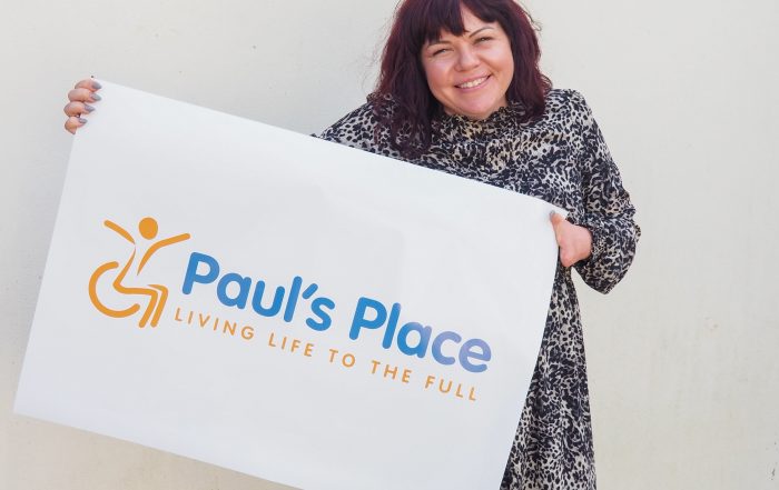 Briony May smiling holding up Paul's Place New Logo on a poster