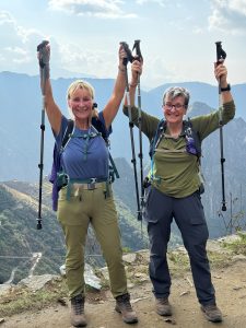 two female hikers on top of Machu Picchu holding their walking poles in the air, celebrating