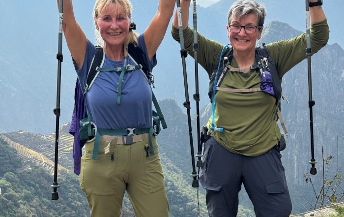 two female hikers on top of Machu Picchu holding their walking poles in the air, celebrating